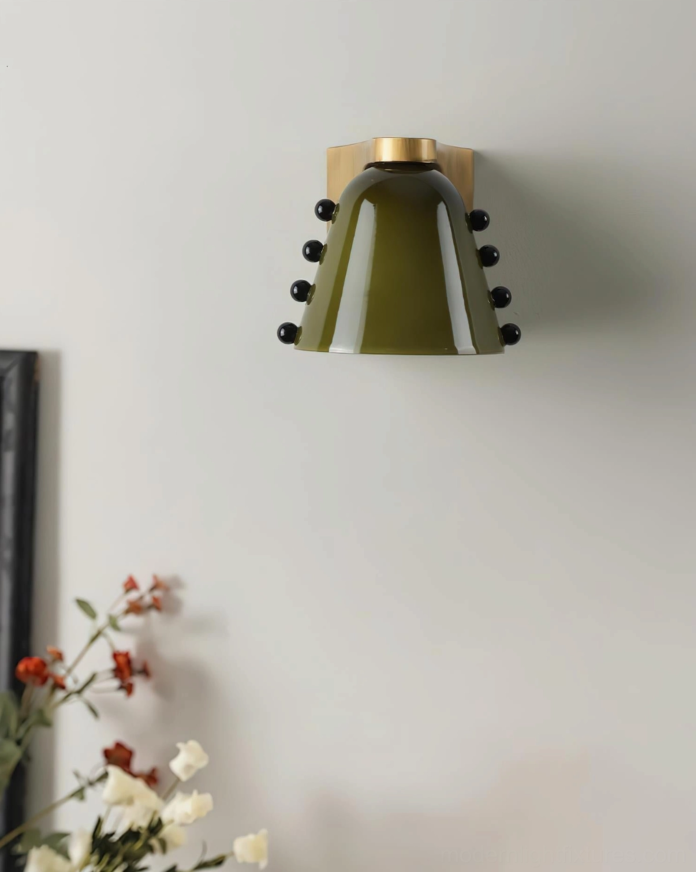 Retro luxury wall sconce with dark green frosted glass cone and brushed brass base against floral decorated wall