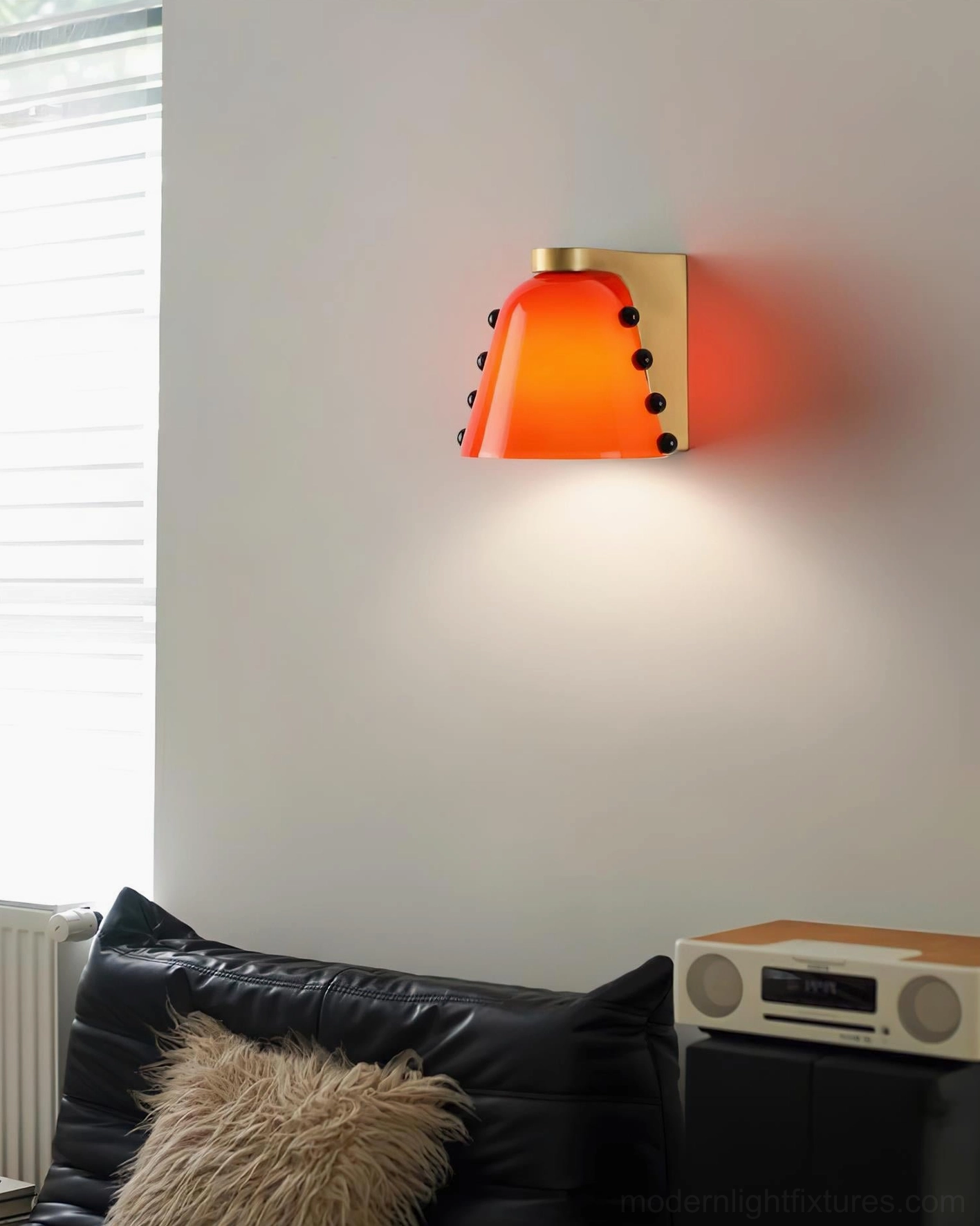 Burnt orange glass wall sconce with brass fixture mounted in luxury living room with leather sofa and audio system