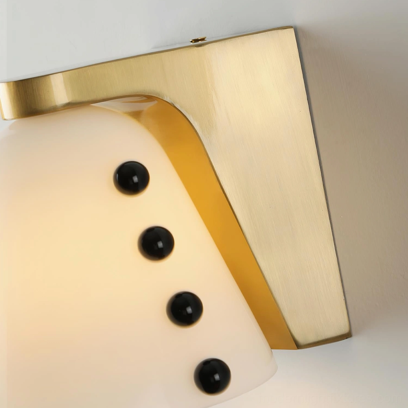 Low-angle close-up of conical wall sconce revealing brushed brass hardware, frosted glass cone, and visible warm internal light with bead accents