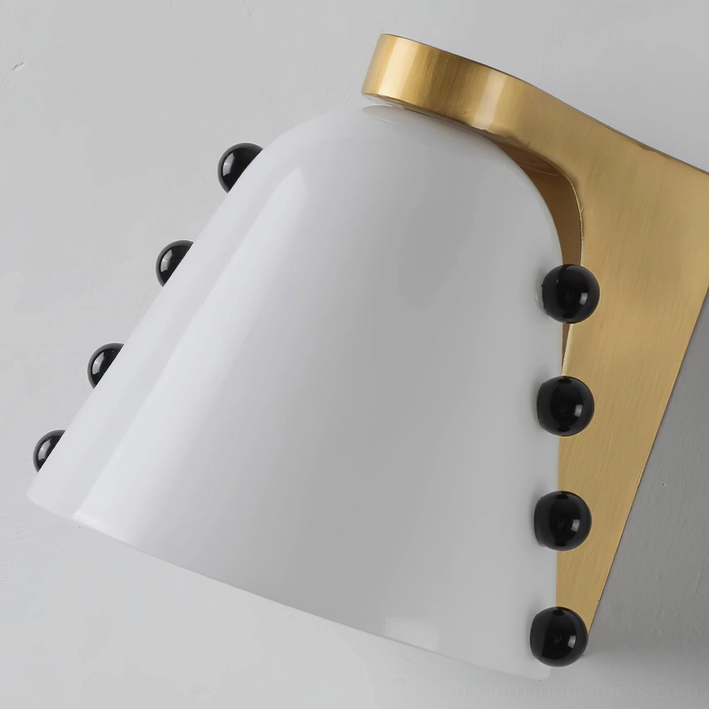 Modern wall sconce close-up side view showing white conical glass shade and brushed brass mounting hardware with black details