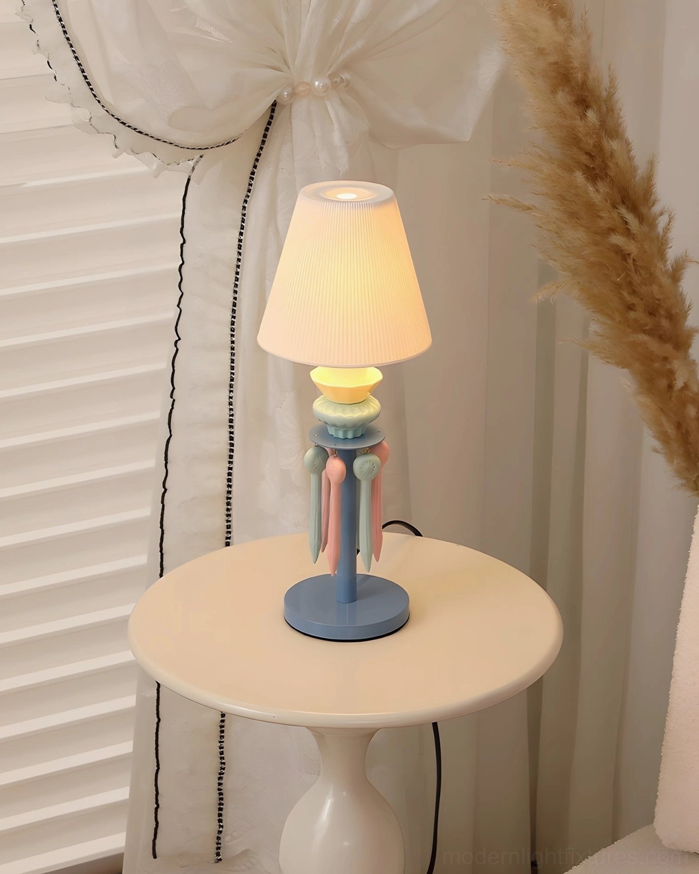 Cielora pastel tassel table lamp with warm yellow pleated shade displayed on small side table with sheer curtains and pampas grass decor