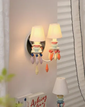 Cielora wall sconce mounted in cozy bedroom setting with warm ambient glow, soft lighting on dual fabric shades and ceramic beads