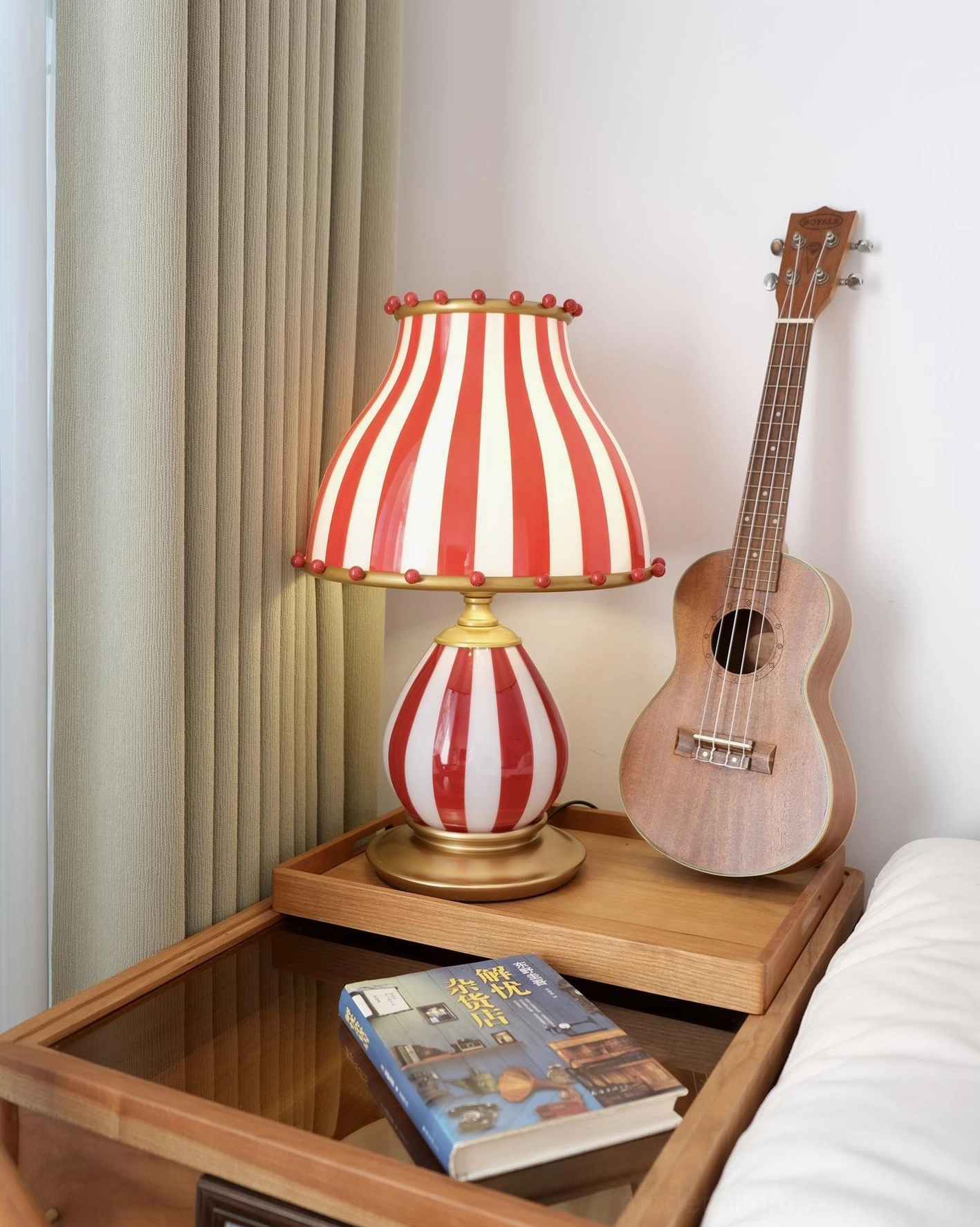 Circus table lamp with pom-poms on bedroom side table with ukulele and reading book