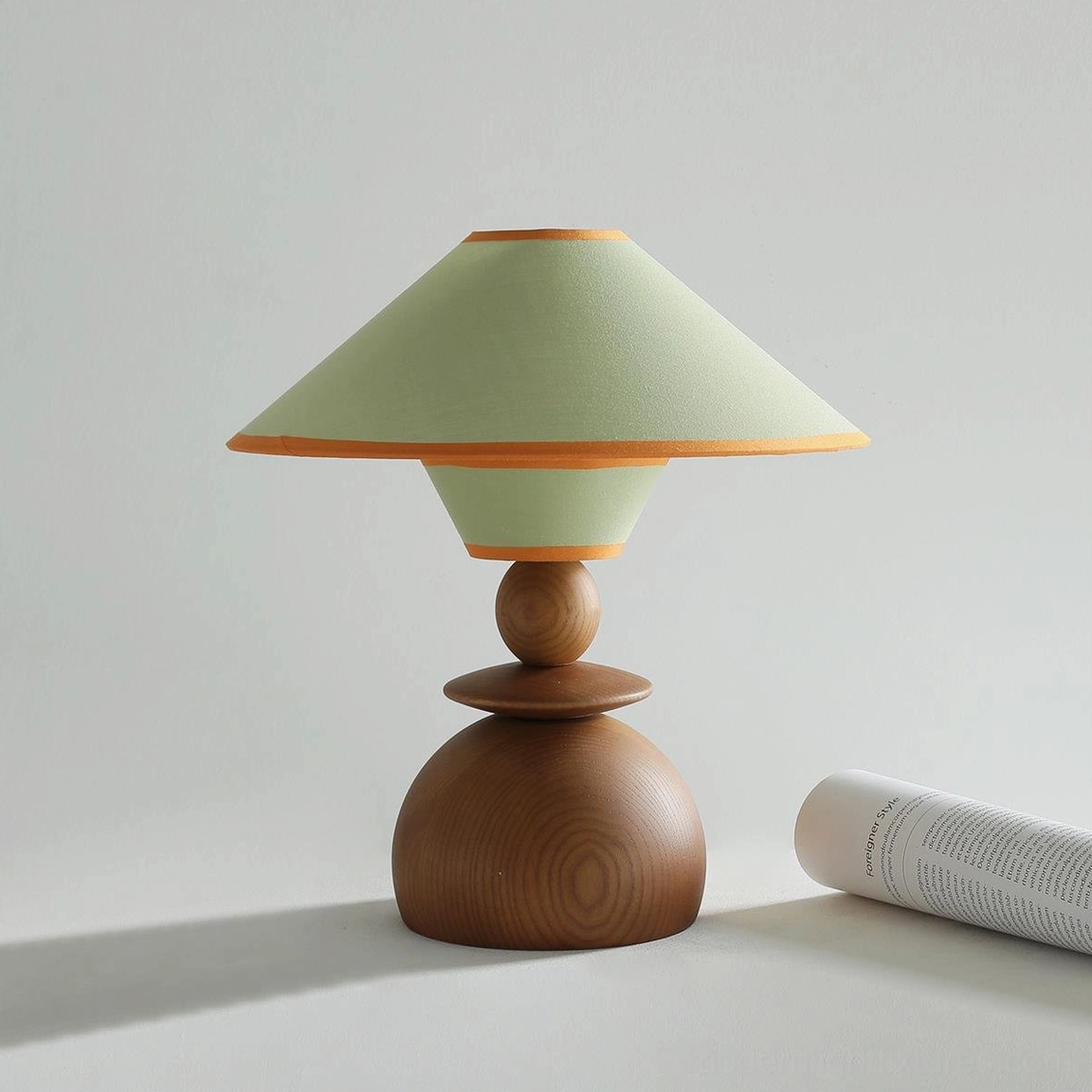 Sage green fabric dome table lamp with orange trim detail and wooden base in contemporary studio setting