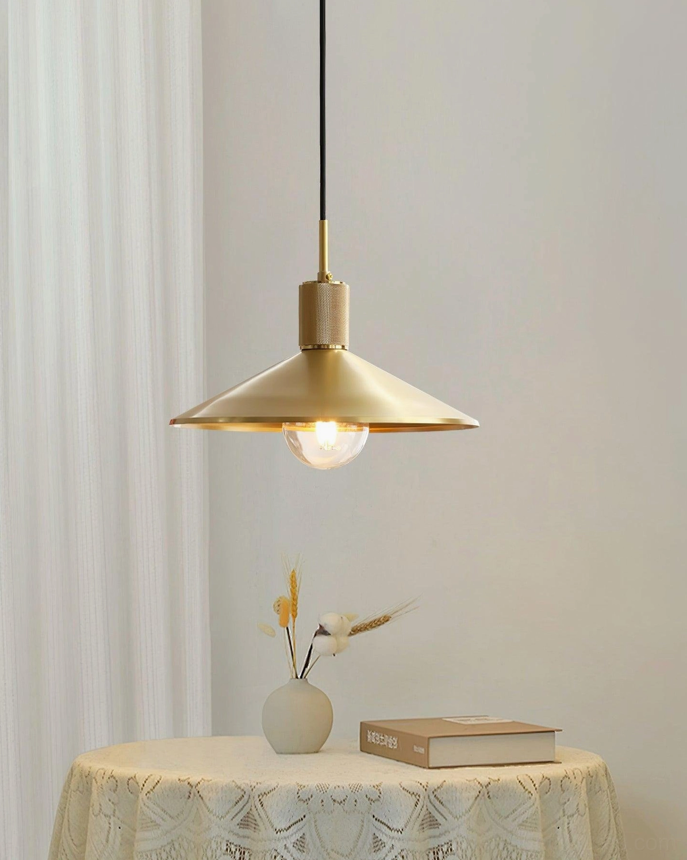 Classic brass pendant light installed in small dining corner with lace tablecloth and minimalist warm neutral decor