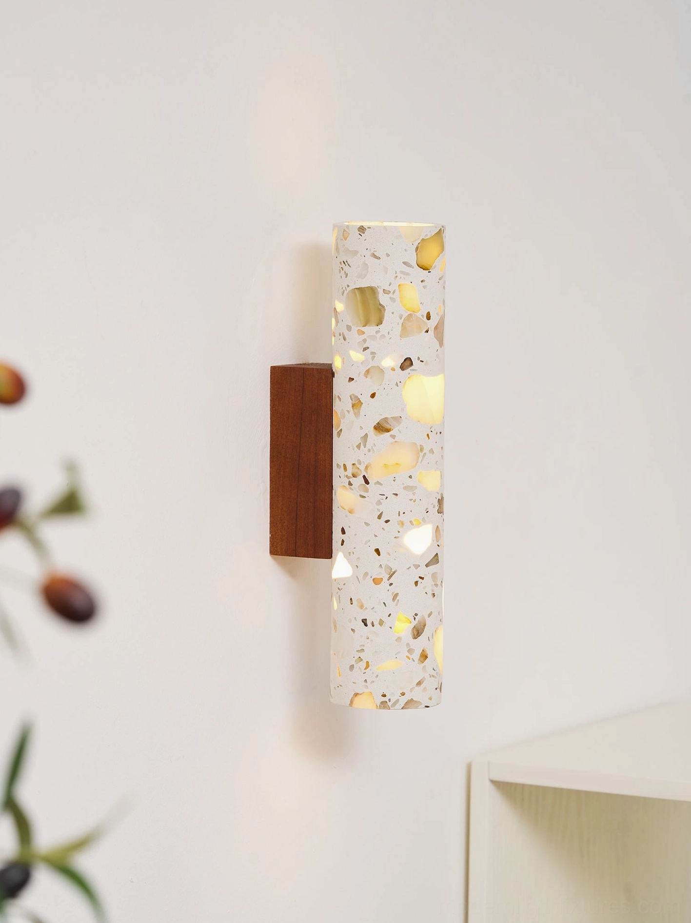 Modern terrazzo sconce mounted on wall showing glowing warm light through stone shade with plant decor nearby