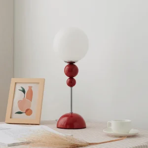 Clavel red spherical table lamp displayed on checkered tablecloth with home décor styling - three-quarter view showing contemporary design in living space