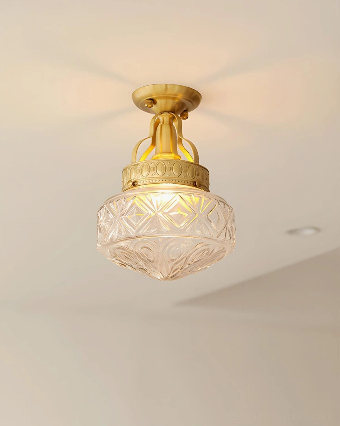 Semi-flush ceiling light with clear carved glass shade illuminated warm, brass gold fitting visible from below