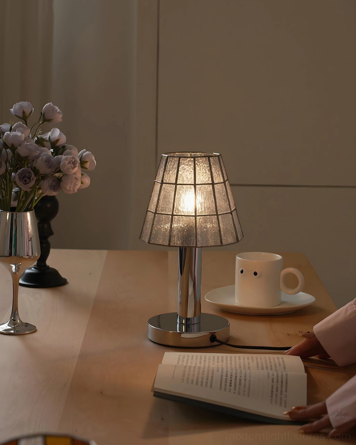 Clear grid pattern stained glass table lamp illuminated on dining table with coffee cup and floral arrangement