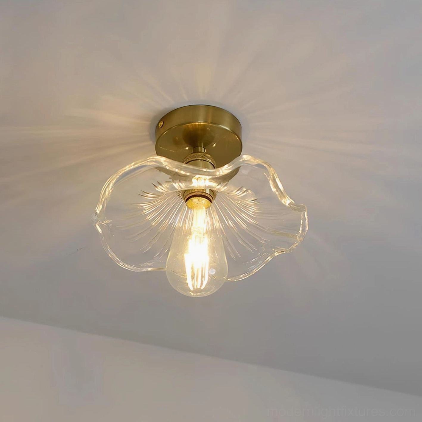 Clear petal-like glass semi-flush ceiling light with warm brass fixture, studio product shot