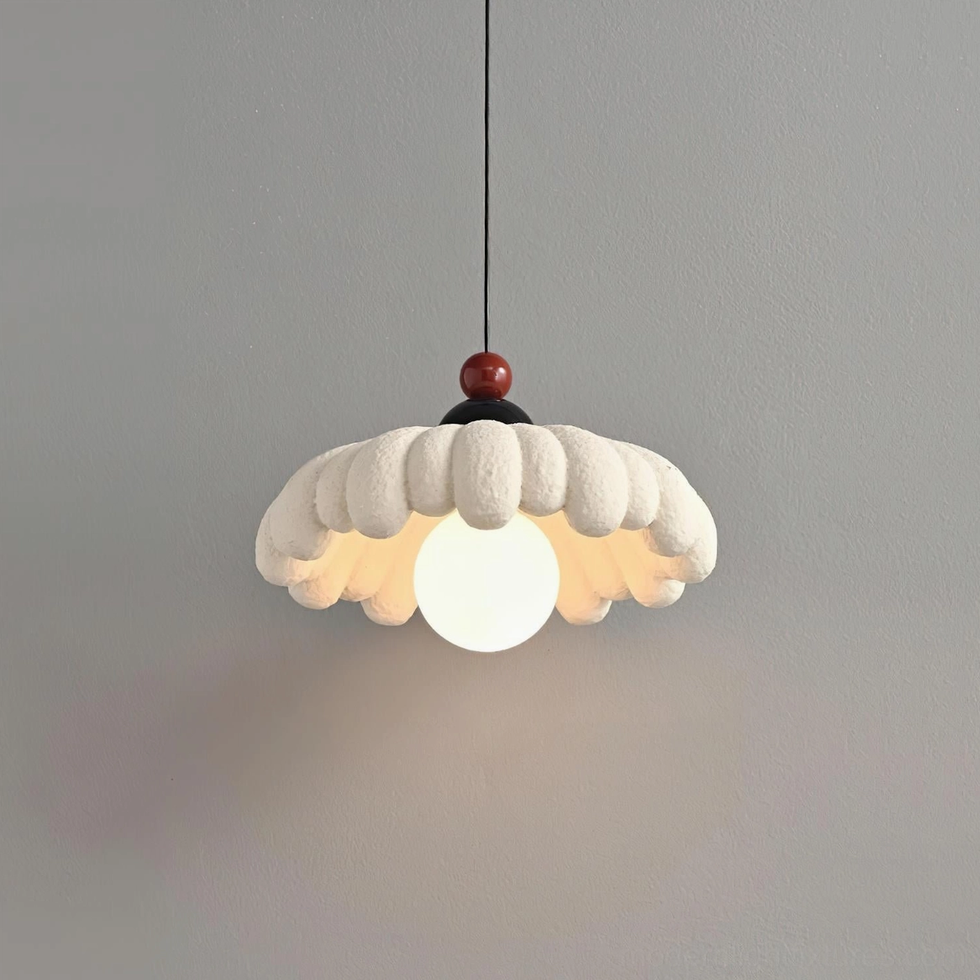 Cloudet pendant lamp with illuminated bulb from below, scalloped shade with red and black decorative hardware, low-angle view