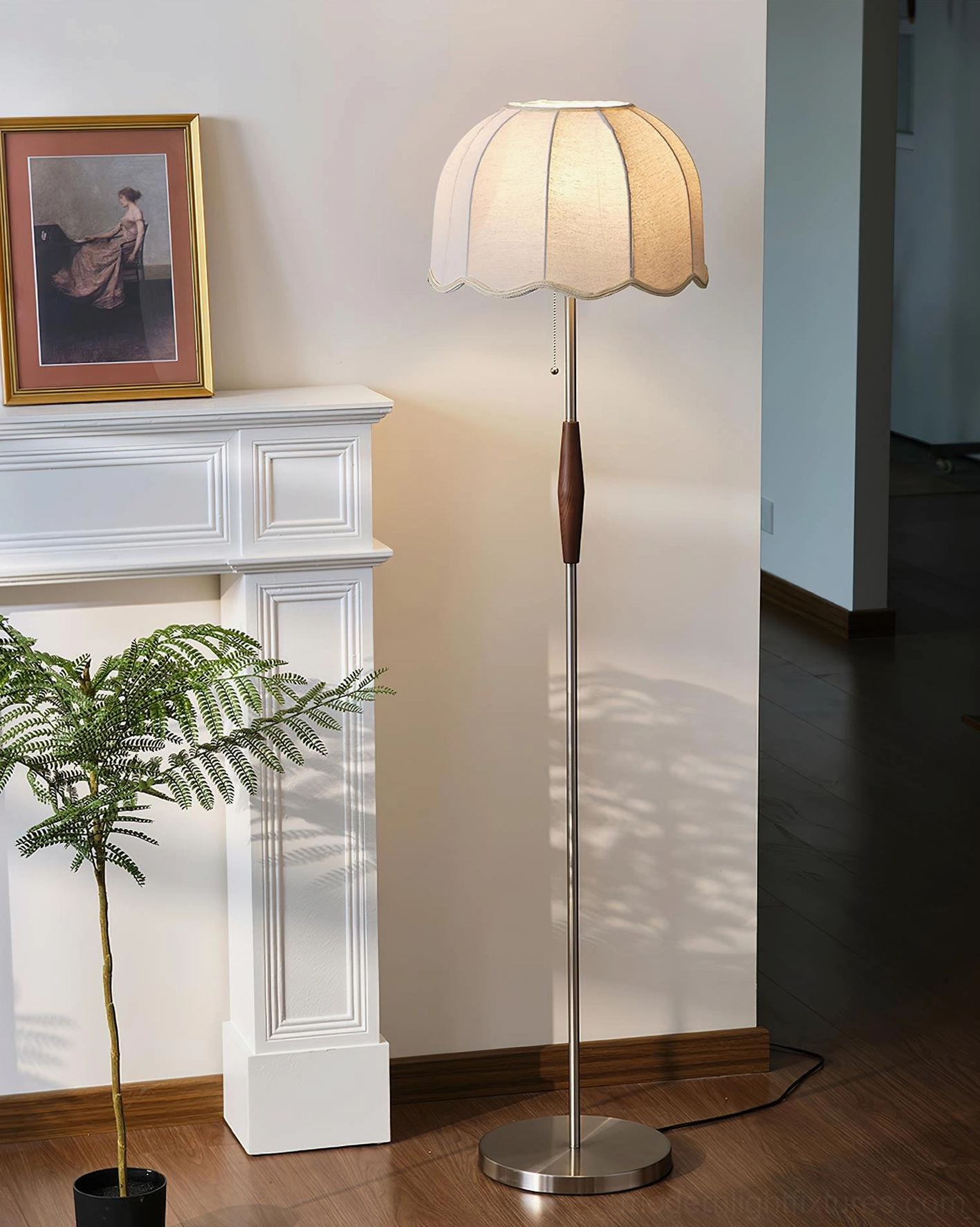 Colette floor lamp with warm glowing scalloped fabric shade, left profile view beside fireplace with fern and framed art