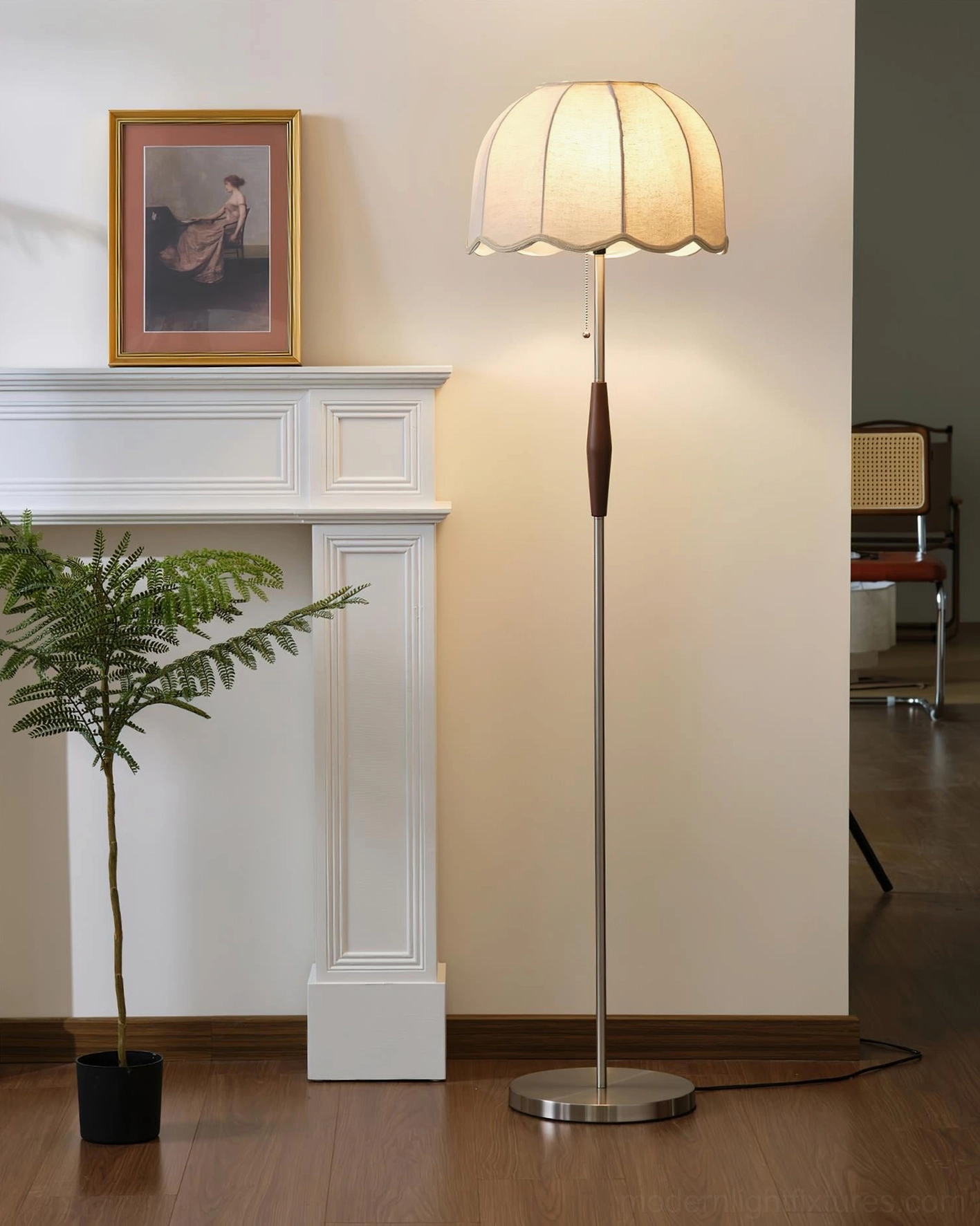 Lit Colette floor lamp with warm diffused light from scalloped fabric shade, positioned beside fireplace with potted plant