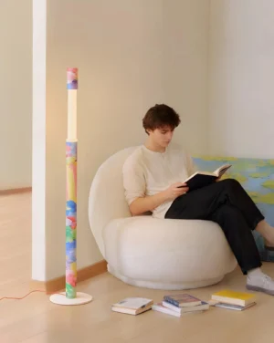 Colorbeam multicolor floor lamp in modern living room beside white lounge chair, side angle showing painted pattern and reading scene styling