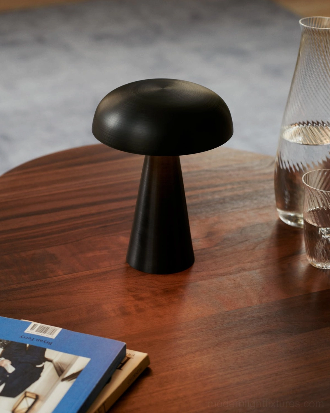 Matte black Como cordless table lamp on wooden side table with glassware and design magazines