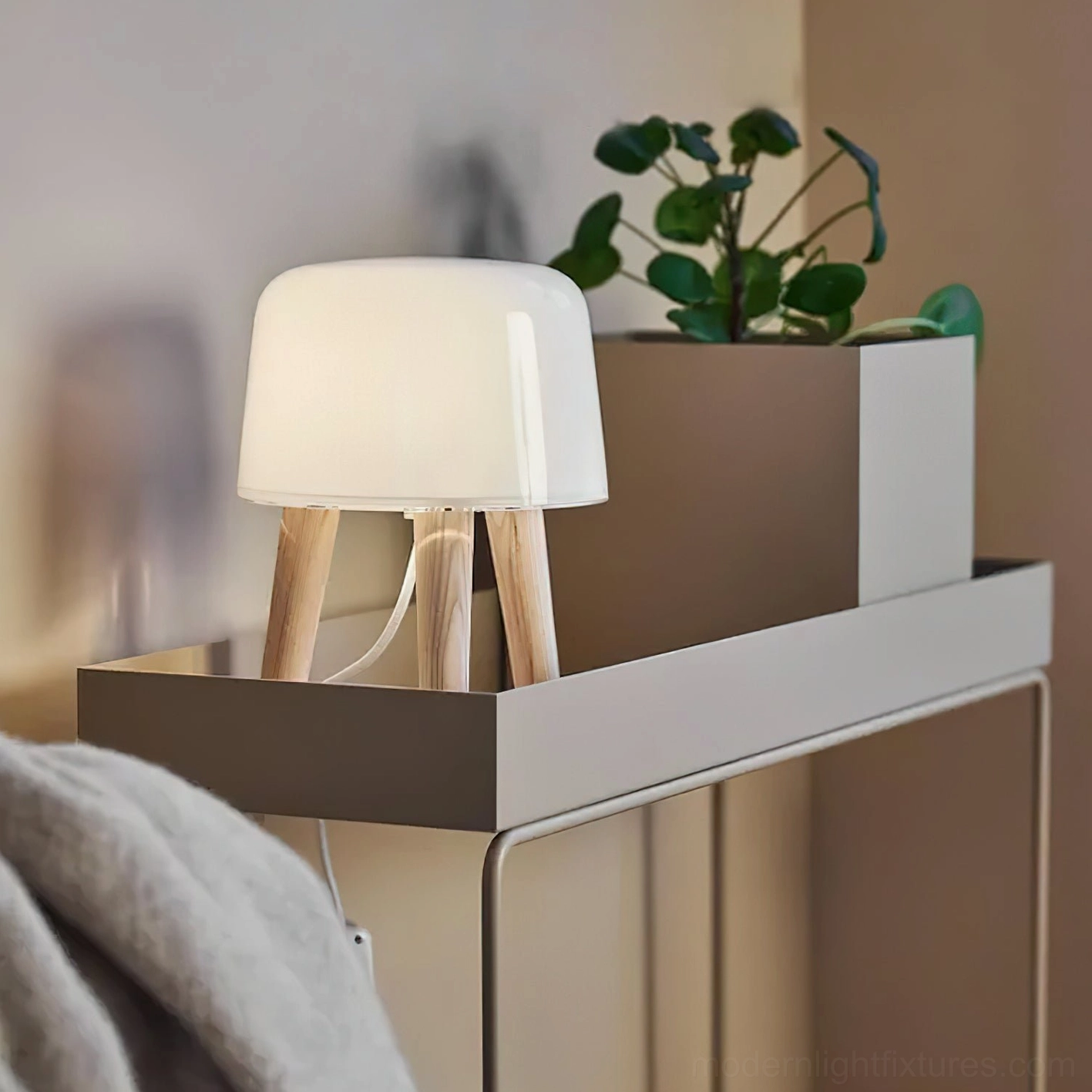 Side angle view of compact milk glass table lamp next to green plant on side table, demonstrating space-saving minimalist design