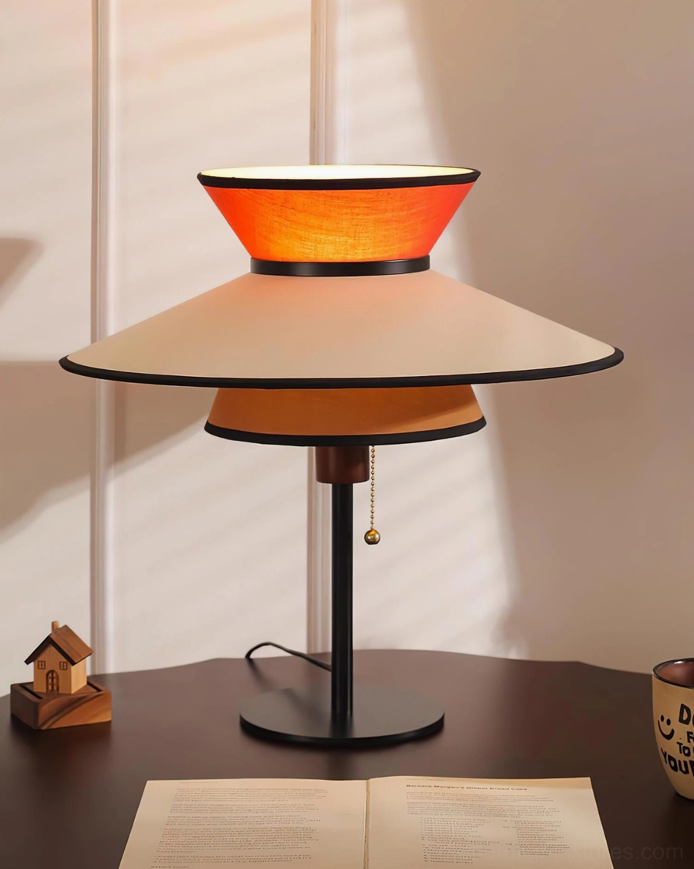 Illuminated modern conical table lamp with warm glowing layered fabric shade on wooden side table featuring black metal base and pull-chain
