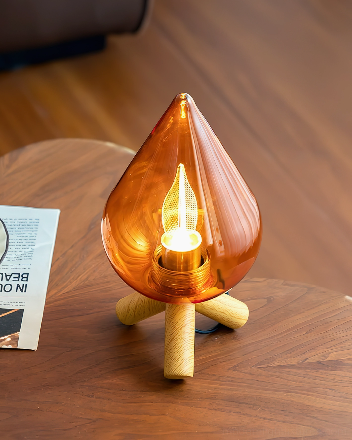 Modern amber teardrop lamp close-up on round wood side table with decorative card, warm LED lighting illuminating glass shade