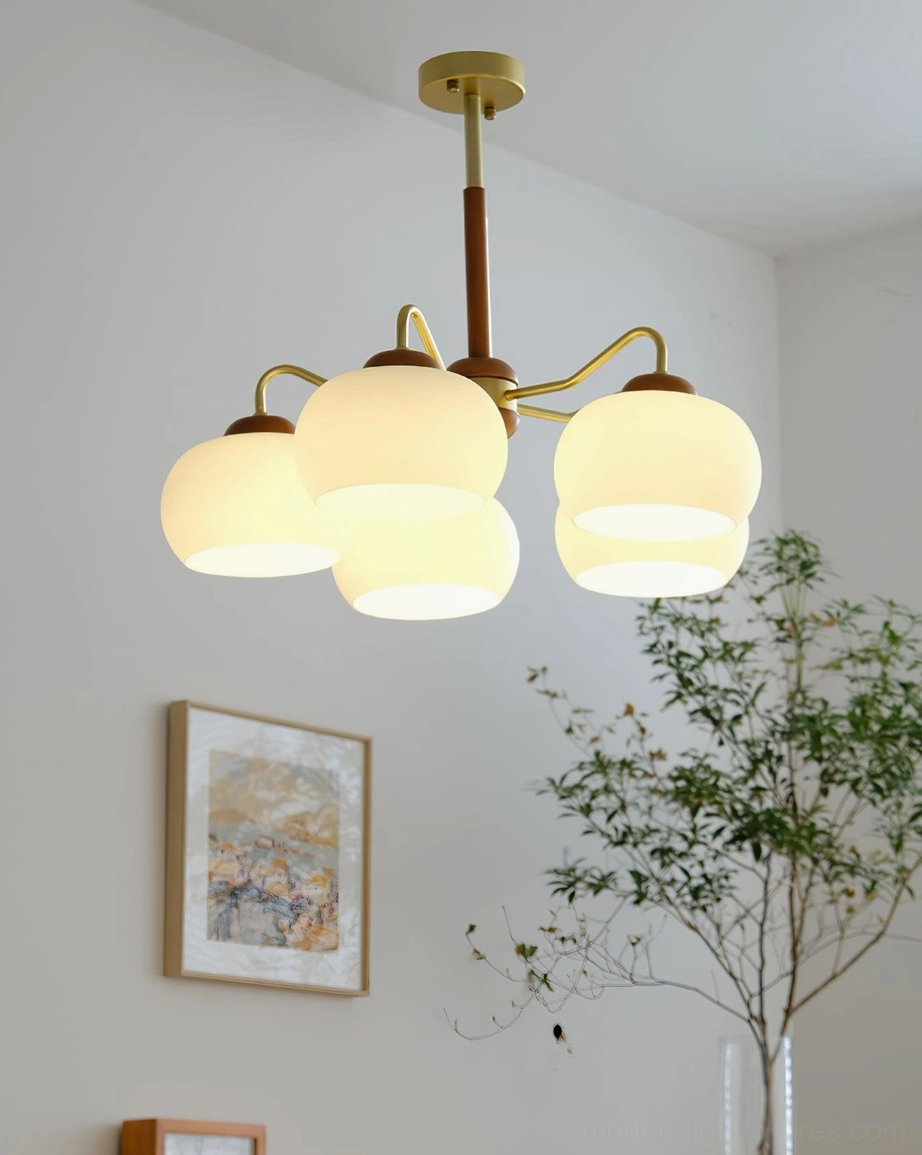 Contemporary pendant chandelier with warm lighting in living room with artwork and potted plants showing gold hardware details