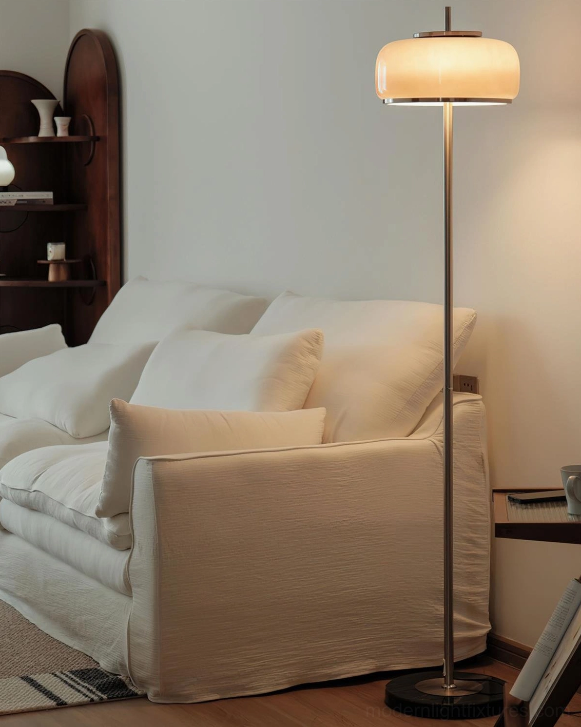 Contemporary floor lamp with warm beige illuminated shade chrome pole and black base in cozy living room interior
