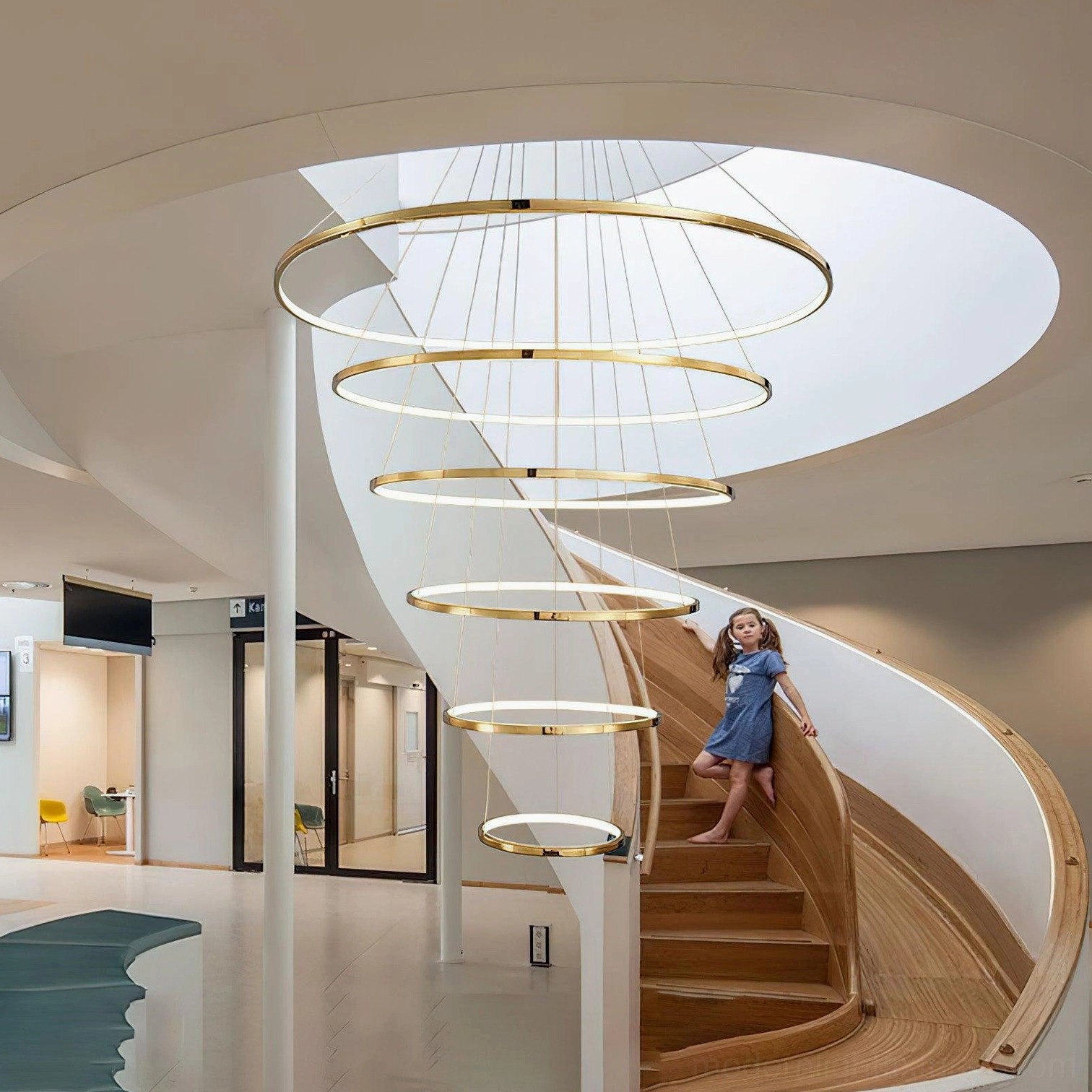 Modern gold tiered ring chandelier hanging in contemporary spiral staircase lobby