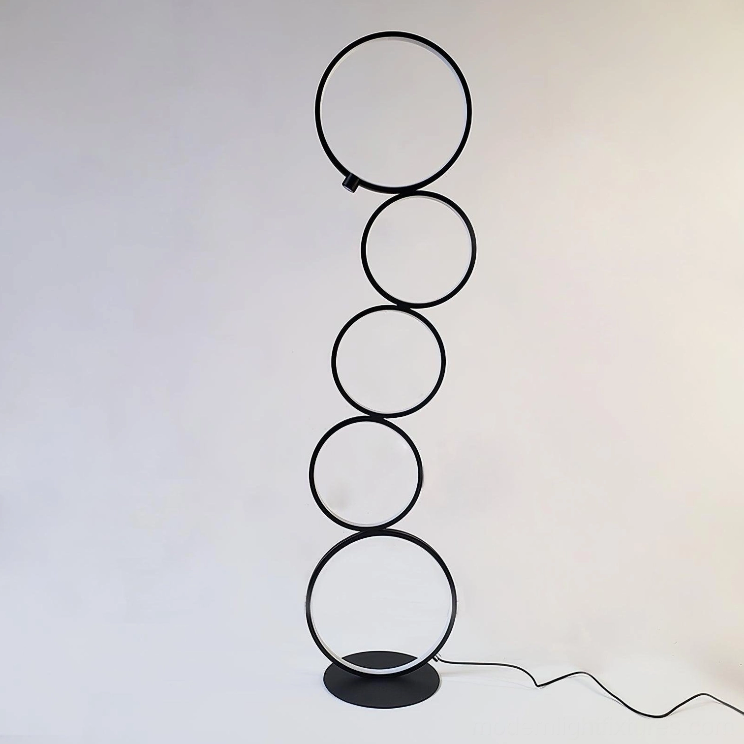 Modern circular floor lamp with metal rings and power cable attached to base against warm studio background