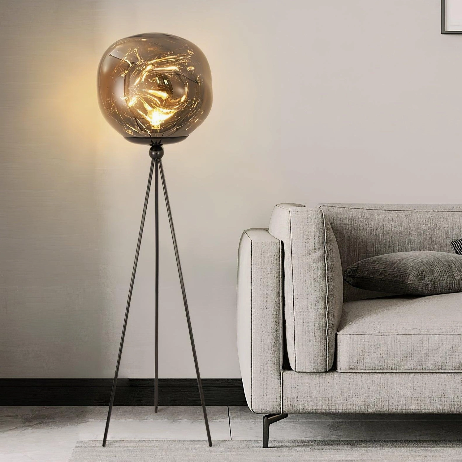 Sleek black tripod floor lamp with molten glass shade beside light gray sofa in contemporary home decor