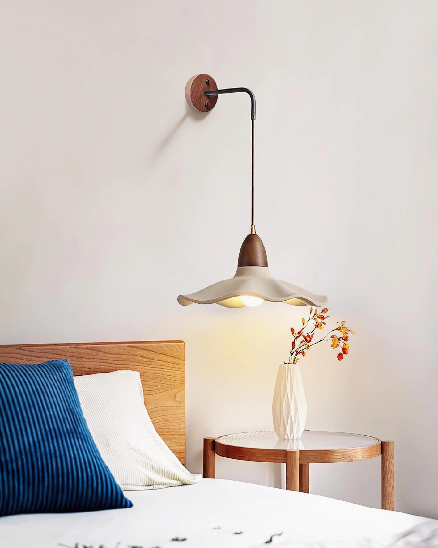 Sculptural wave wall sconce creating warm ambient lighting in master bedroom with wooden bed frame and floral decor