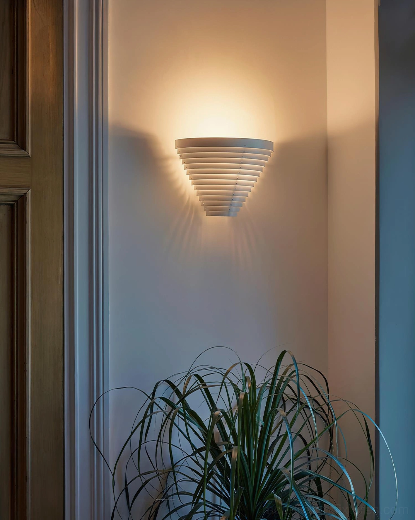 Modern wall sconce in entryway with green plant decor, geometric light patterns illuminating wall surface