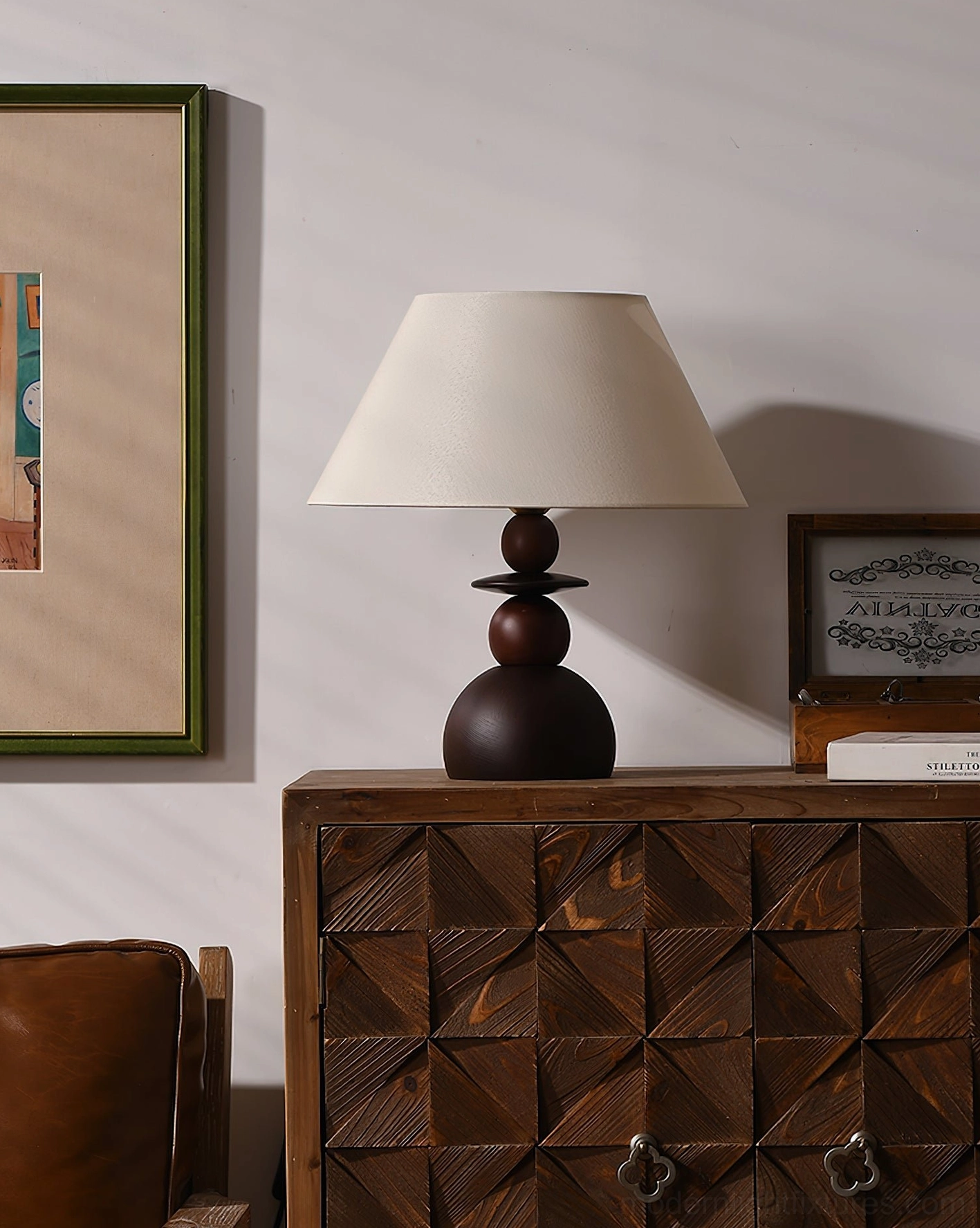 Modern table lamp with off-white fabric shade and dark stacked walnut wood base on carved wooden dresser