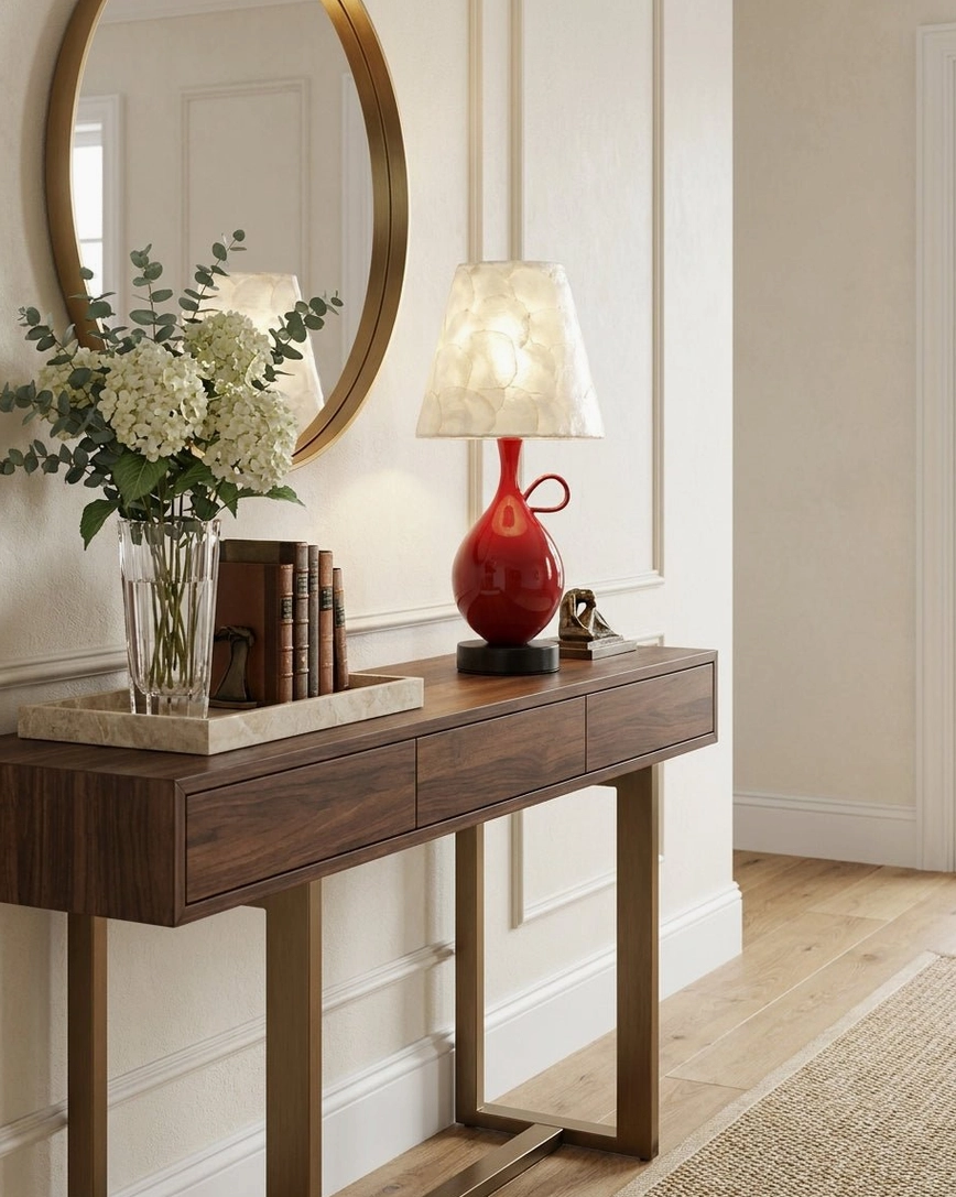 Coravie table lamp on wood-and-metal console table in formal entryway paired with floral arrangement and round wall mirror