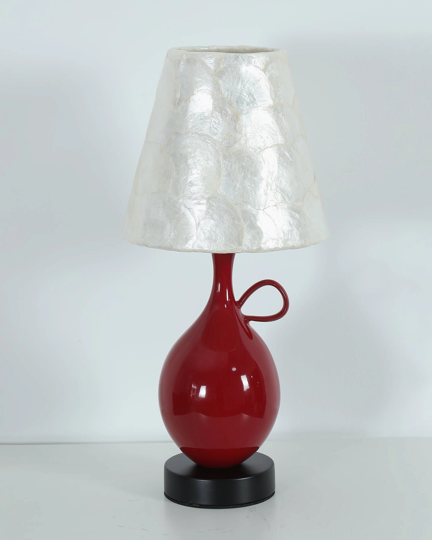 Close-up detail of Coravie red ceramic gourd base showing glossy red glaze finish and small loop handle with black round foot