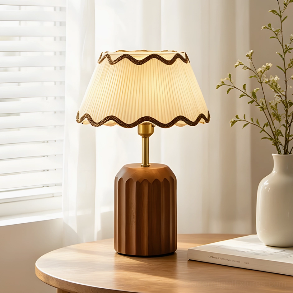 Cordelia pleated fabric table lamp on sunlit wooden side table, daisy shade with scalloped brown trim and fluted base paired with vase and book