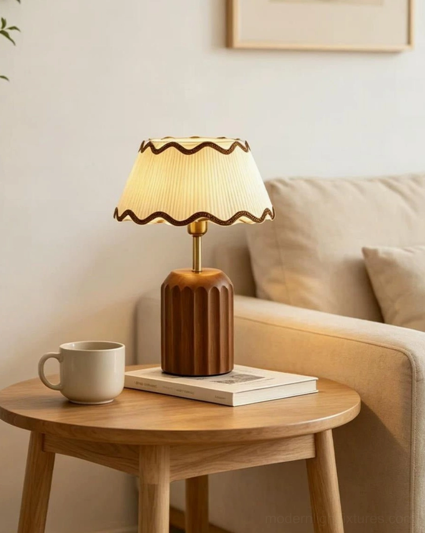 Cordelia warm white table lamp beside living room sofa, fluted walnut base with pleated shade casting soft ambient glow on coffee table