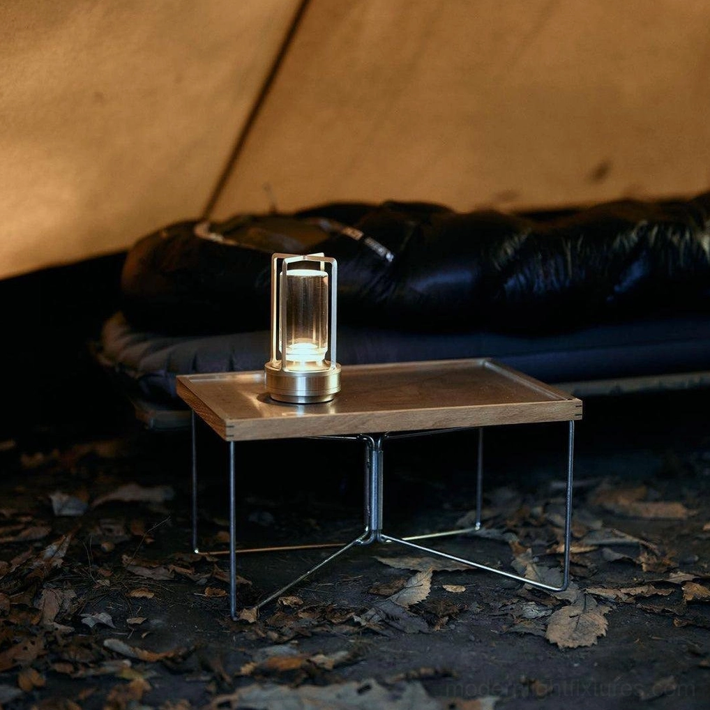 Gold cordless LED table lamp placed on metal side table in outdoor camping tent lounge scene, lit ambient light