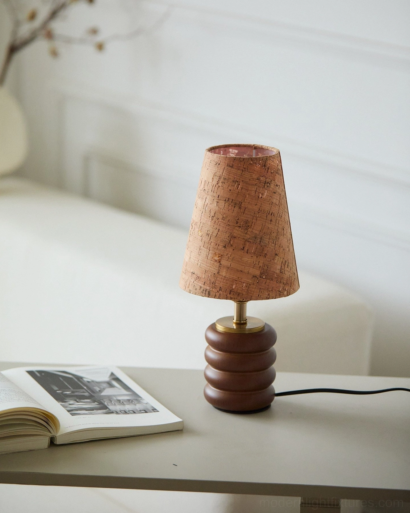 Natural cork shade table lamp with walnut wood base on minimalist white side table beside magazine