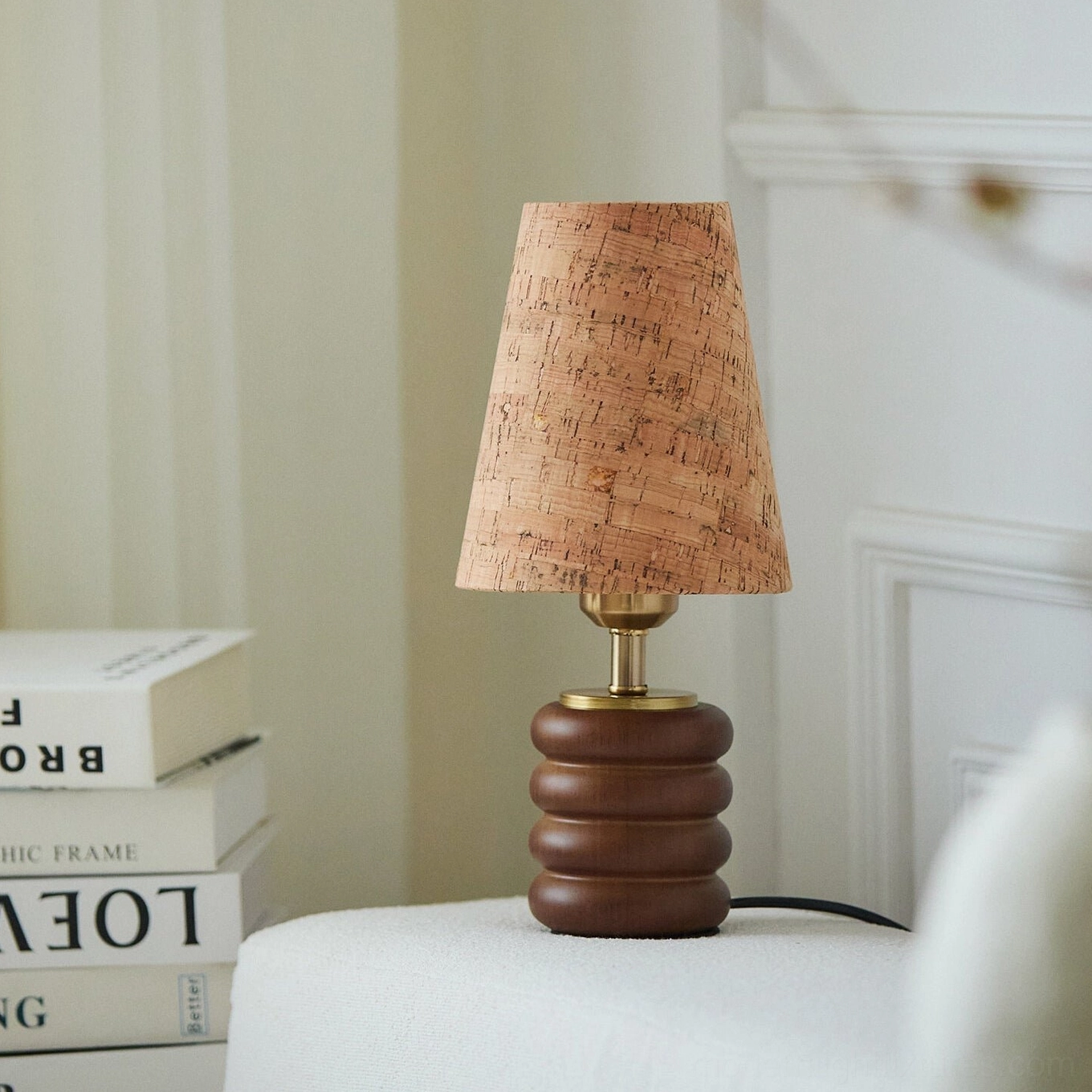 Japandi table lamp with stacked walnut base and cork shade placed on decorative books beside bed