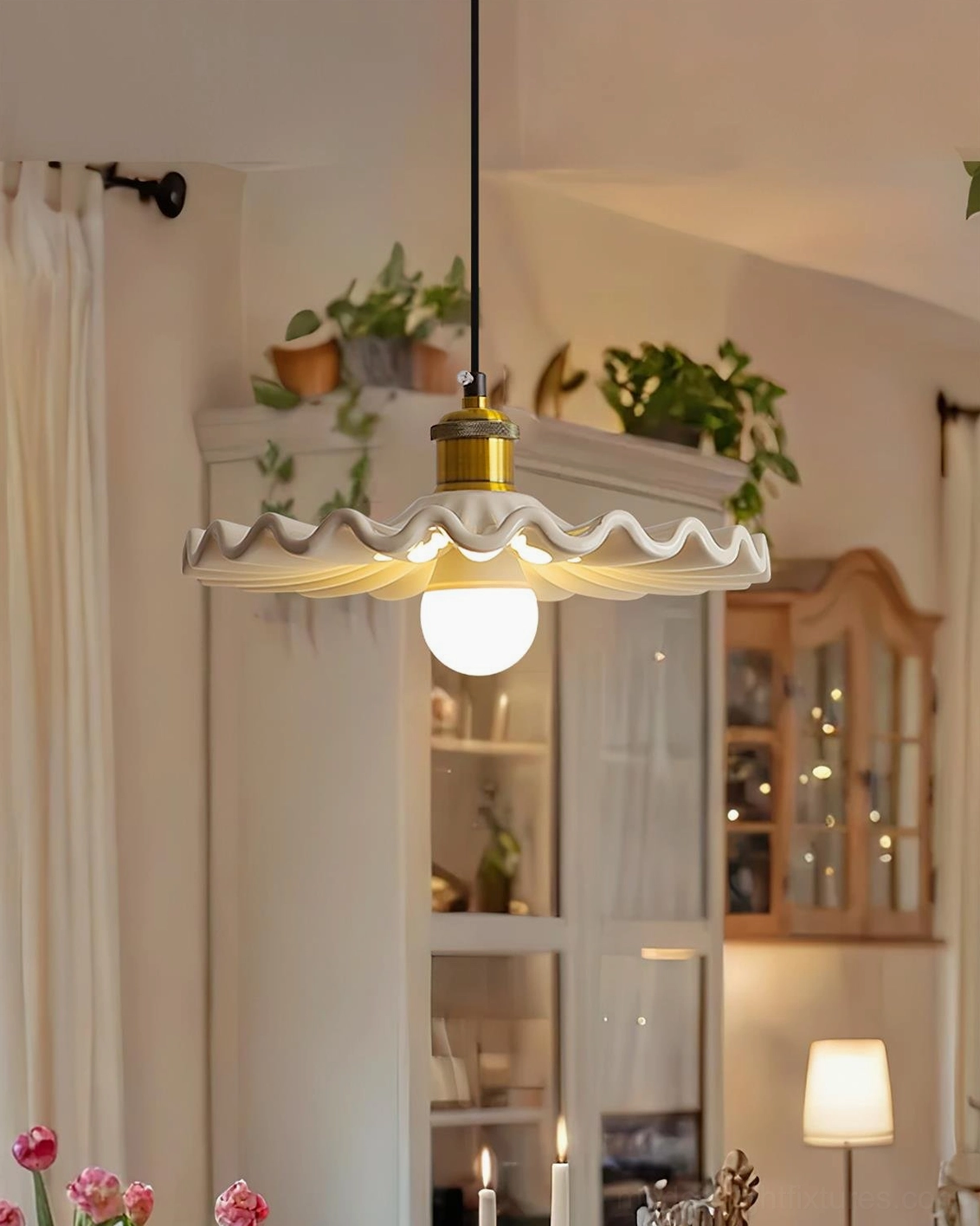Corolla pendant lamp hanging in cozy dining and living space with plants and wooden cabinetry, lit detail