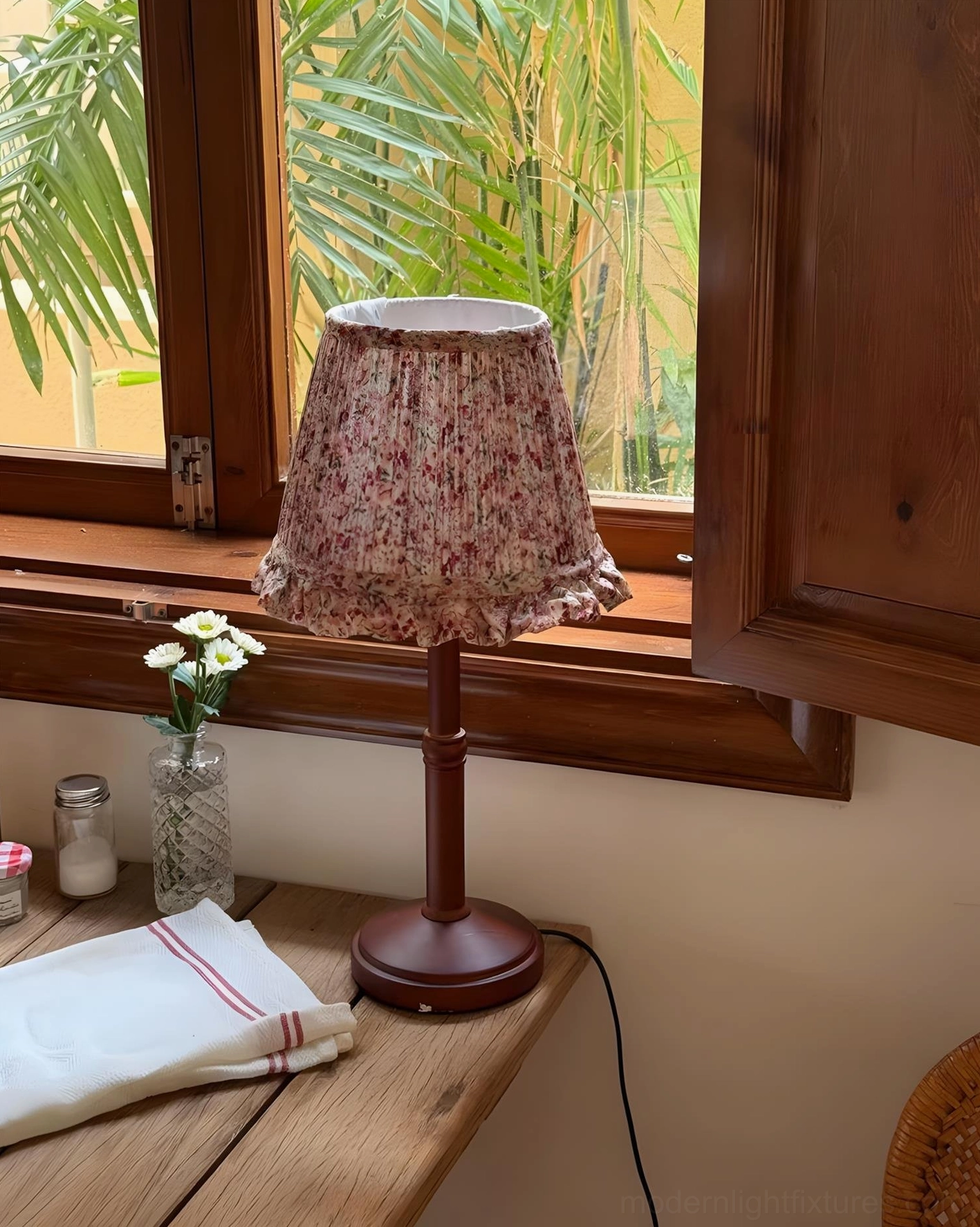 Cottage floral table lamp on wooden table by brown window with glass vase and linen napkin