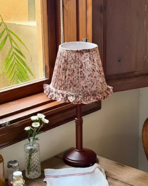 Cottage table lamp placed on dining table by vintage window with flower vase and linen napkin, side view