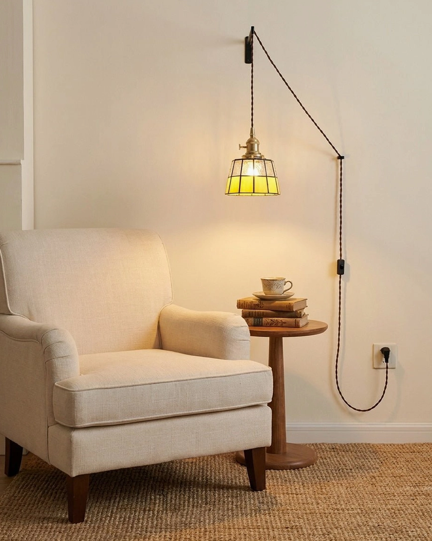 Brass and amber stained glass pendant light hanging in living room reading corner above upholstered armchair creating intimate vintage aesthetic