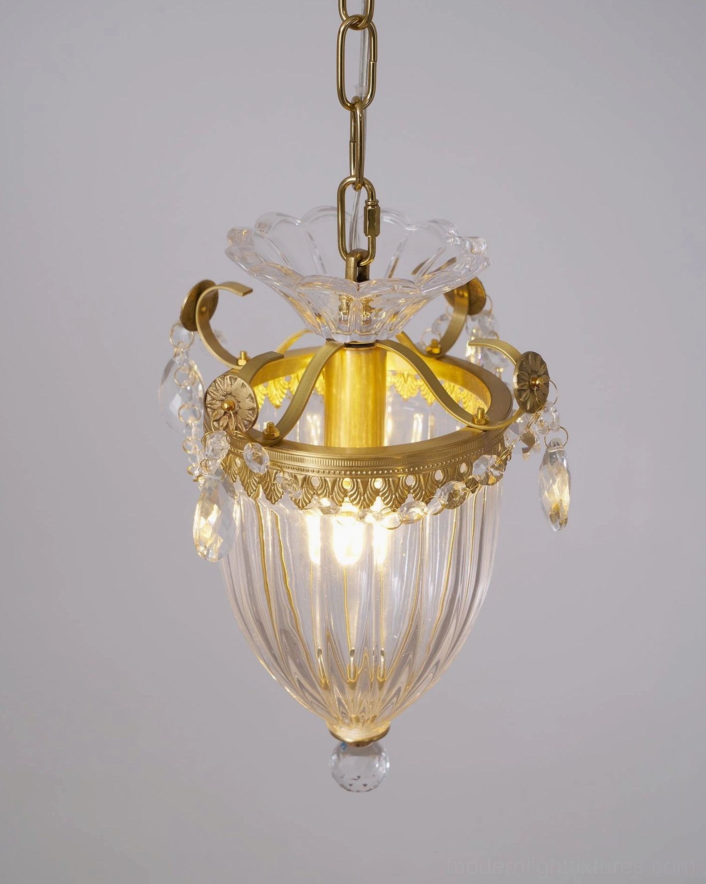 Three-quarter view of illuminated brass crystal pendant light with ornate design and clear shade