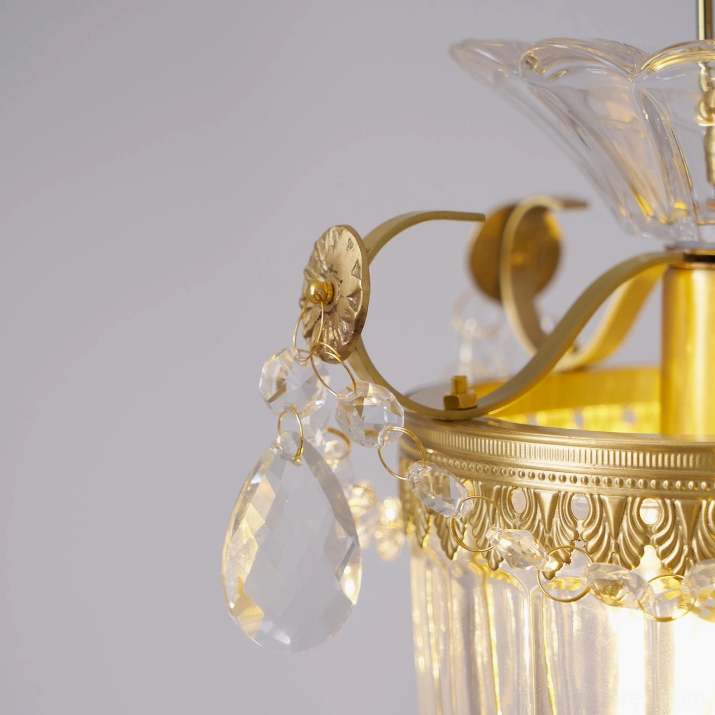 Top-down close-up of floral brass trim and faceted crystal pendants on vintage light fixture
