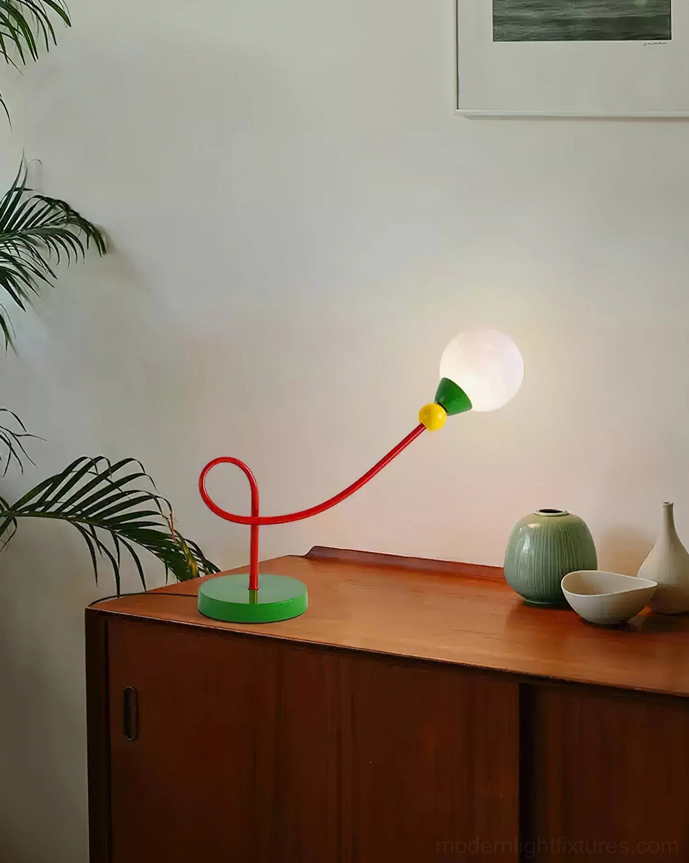 Artistic curved arm lamp displayed on wooden cabinet with green ceramic home decor accessories