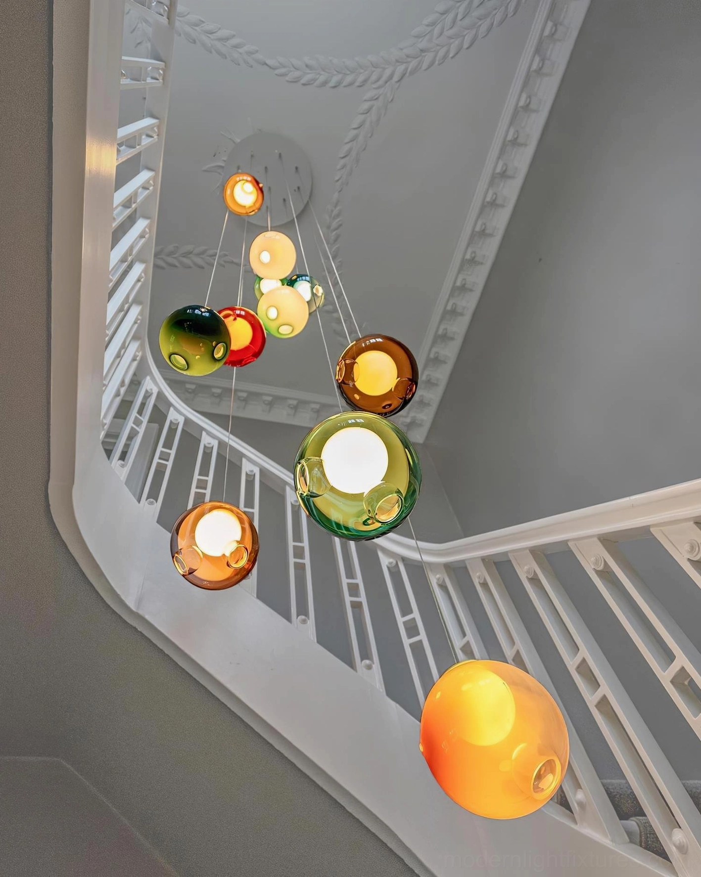 Asymmetric glass globe cluster chandelier hanging in curved luxury residential stairwell, contemporary pendant lighting design