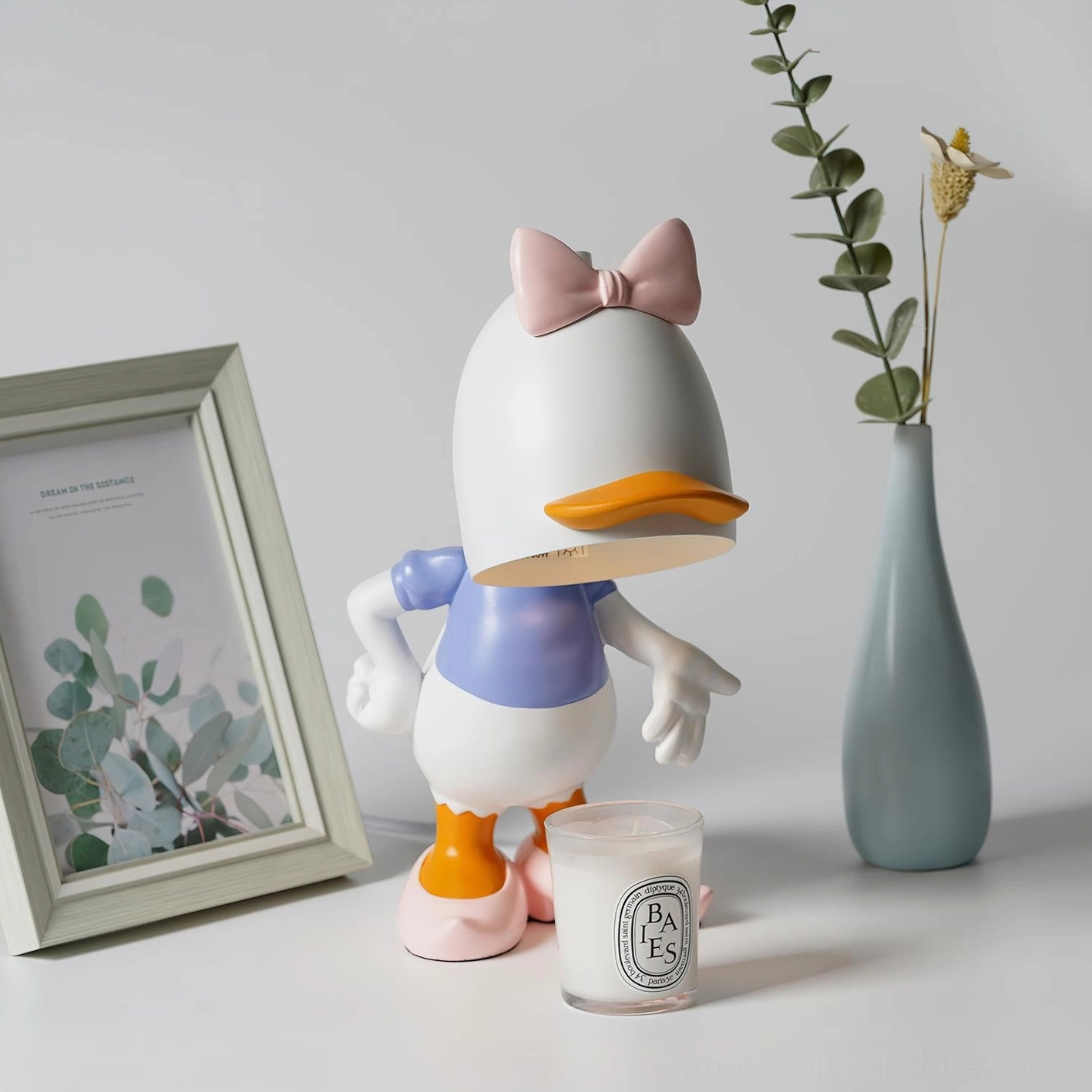 Daisy Duck pink and white candle warmer lamp with scented candle melting demonstration in stylized home décor setting with framed photo
