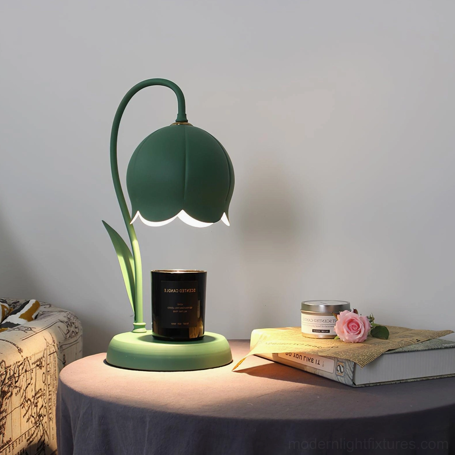Lit dark green lily candle warmer lamp three-quarter front view on bedside table with art print and flower vase