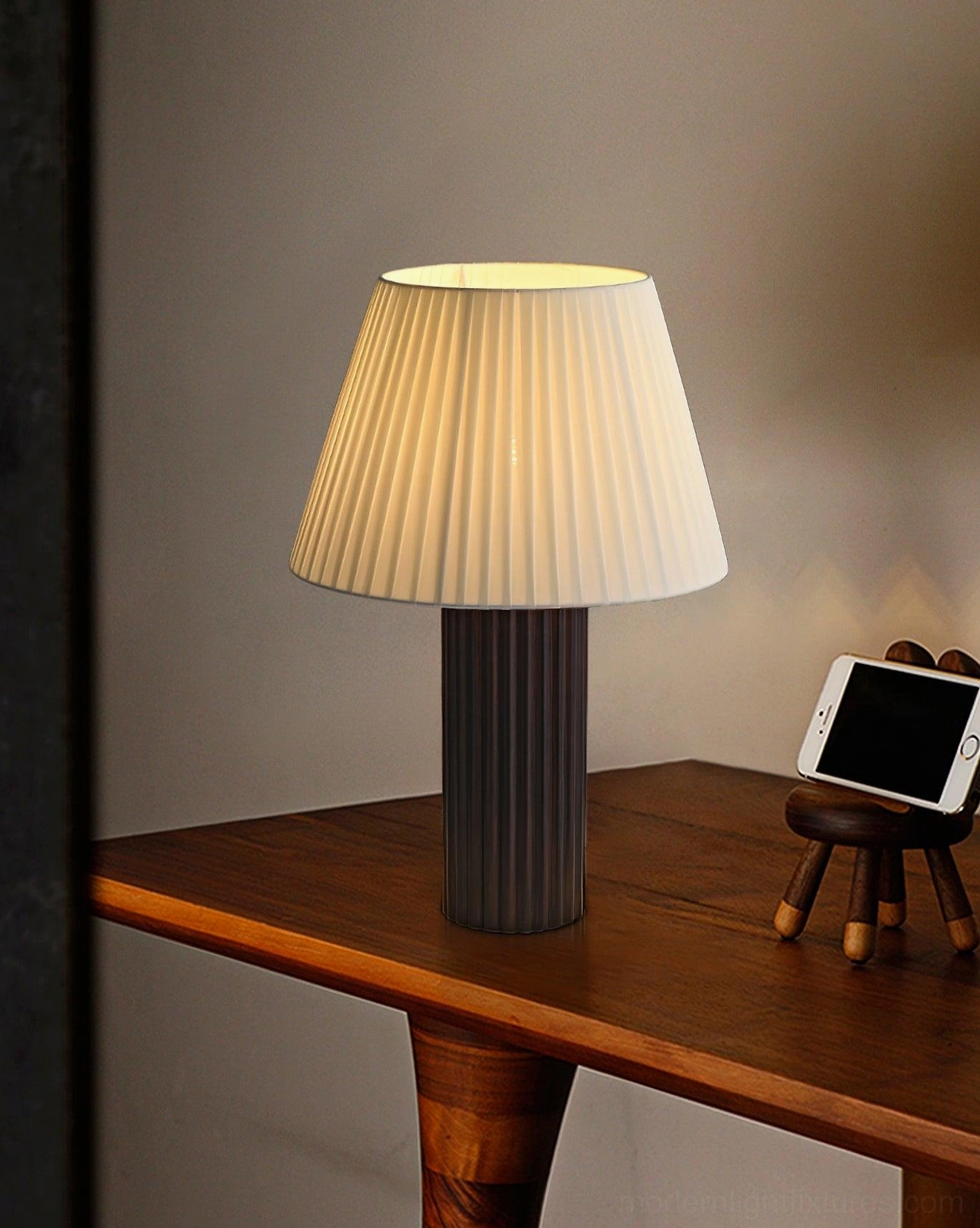 Dark ribbed base modern table lamp with white pleated shade on wooden desk with small desktop ornaments in retro minimalist home office style