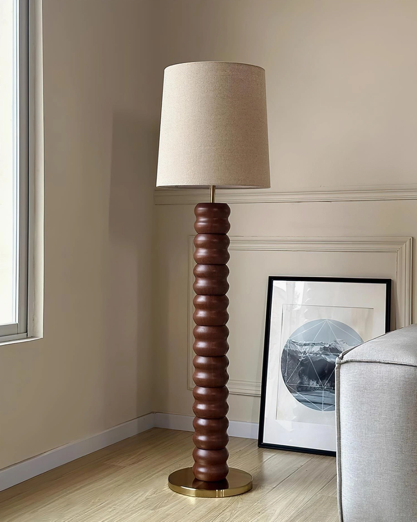 Dark brown stacked wood floor lamp with beige linen shade and brass base in living room with artwork