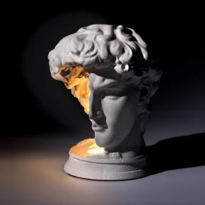David bust table lamp illuminated from within, warm ambient light glowing from hollowed interior, front three-quarter view in dark studio setting